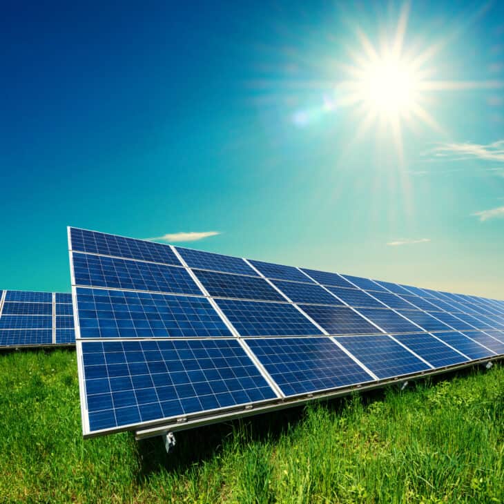 Solar panel on blue sky background. Green grass and cloudy sky. Alternative energy concept