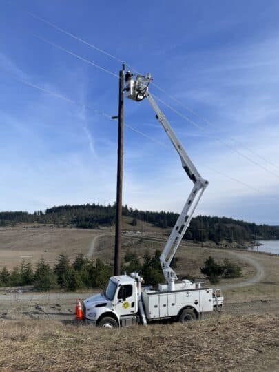 Un operario de líneas de OPALCO trabaja en un tramo de línea desde la grúa cesta en la cantera de grava de Island Rec.
